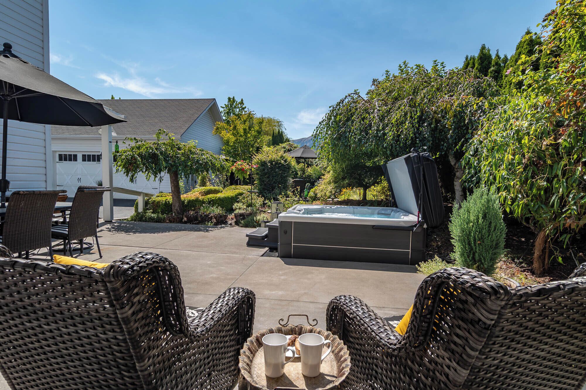 An outdoor patio area with wicker furniture, a hot tub, and a well-maintained garden.
