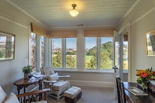 Una habitación con un amplio ventanal, una silla de madera, una mesita con un vaso y vistas a un paisaje.