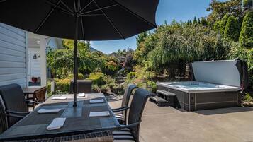 Um pátio externo com mesa, cadeiras, uma banheira de hidromassagem e um guarda-sol grande.
