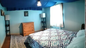 Een slaapkamer met een bed, een dressoir en een nachtkastje met een lamp.