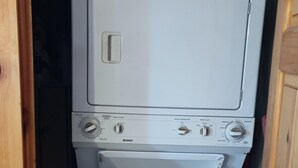 Een compacte, witte wasmachine in een houten kastje met een klein raampje.