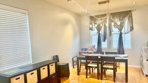 A modern dining area with a wooden table and chairs, a black storage unit with drawers, and a large window with sheer curtains. - Spacious & Cozy Home 3BD 2BA Near SF (Daly City)