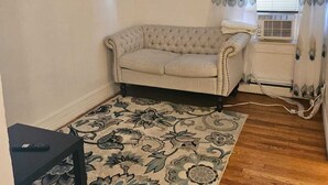 En stue med en beige sofa, et mønstret tæppe og et vindue med gardiner.