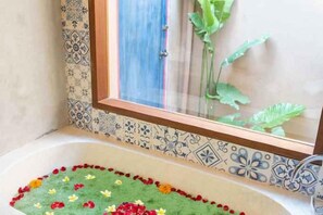 A bathtub with a floral arrangement and a window with a view of a plant. - The Compass Rose Ubud (Bali)