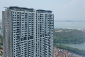 A high-rise building with multiple floors, large windows, and a view of a body of water and greenery in the background. - Aesthetic 2BR @ Urban Suite (Infinite Pool & Gym) (George Town)
