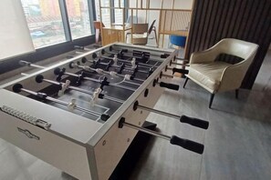 A foosball table in a room with a view through large windows, a chair, and a table. - Aesthetic 2BR @ Urban Suite (Infinite Pool & Gym) (George Town)