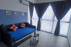 A room with a blue sofa, two British flags pillows, a small table, and a window with curtains. - Aesthetic 2BR @ Urban Suite (Infinite Pool & Gym) (George Town)