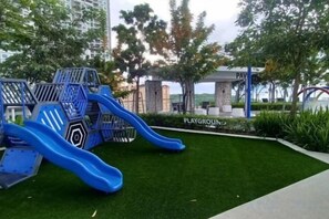 A playground with a slide and climbing structures, surrounded by green artificial grass and trees. - Aesthetic 2BR @ Urban Suite (Infinite Pool & Gym) (George Town)