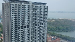 A high-rise building with multiple floors and balconies, overlooking a body of water and greenery. - Aesthetic 2BR @ Urban Suite (Infinite Pool & Gym) (George Town)