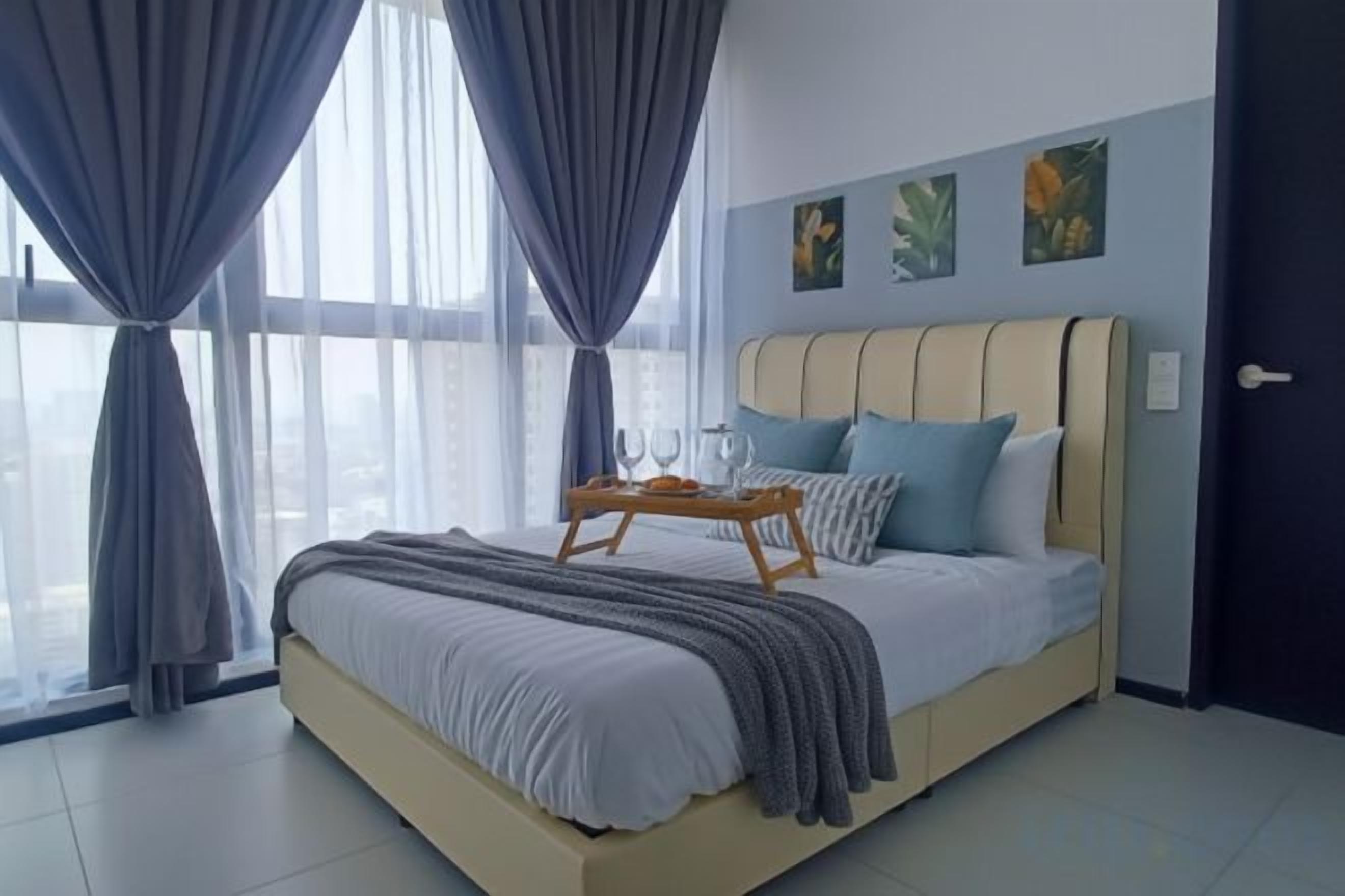 Une chambre à coucher moderne avec un grand lit, des rideaux, une table de chevet avec des lunettes et des œuvres d’art accrochées au mur.