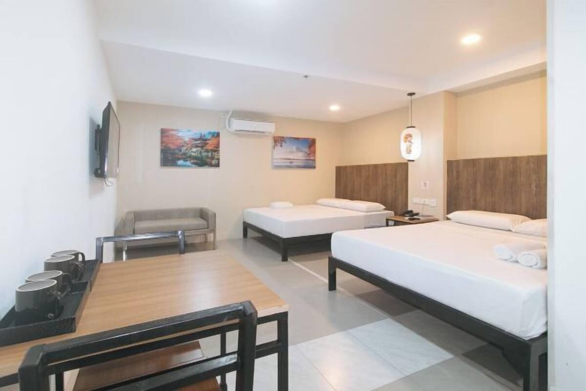 A hotel room with two beds, a desk, a chair, and a TV.