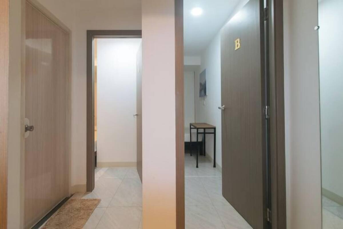 A hallway with a wooden door on the left, a small table with chairs in the center, and a dark door on the right.