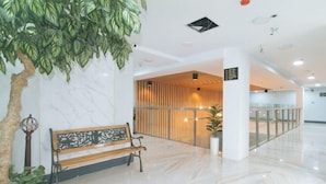 Un hall d’entrée moderne avec un sol en marbre, un banc en bois, un comptoir d’accueil et un grand arbre artificiel.