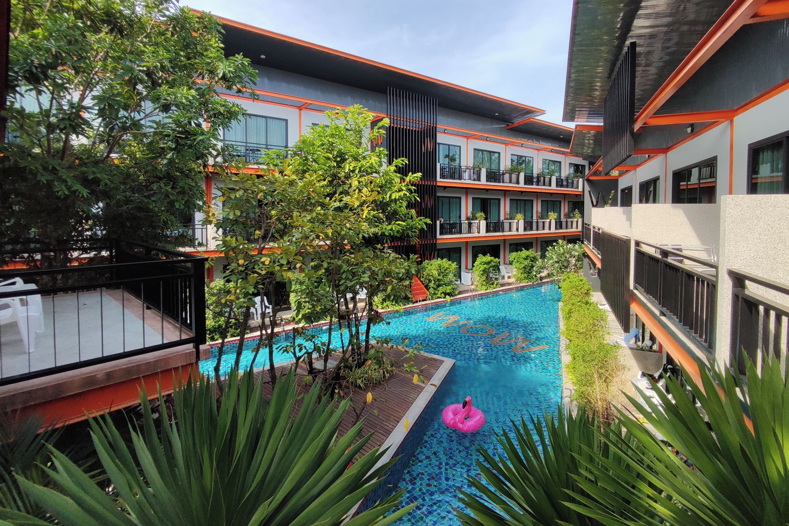 A modern hotel with a swimming pool, outdoor seating, and lush greenery.