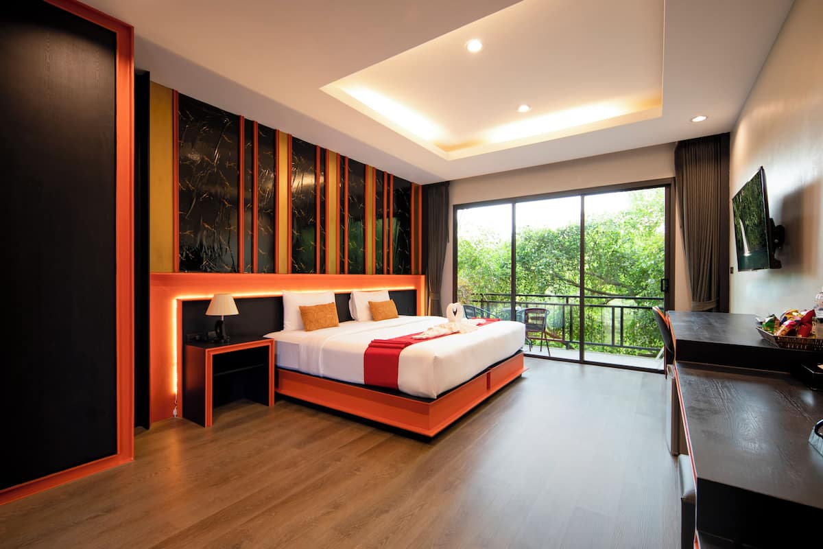 A modern hotel room with a large bed, a desk, and a balcony with a view of greenery.
