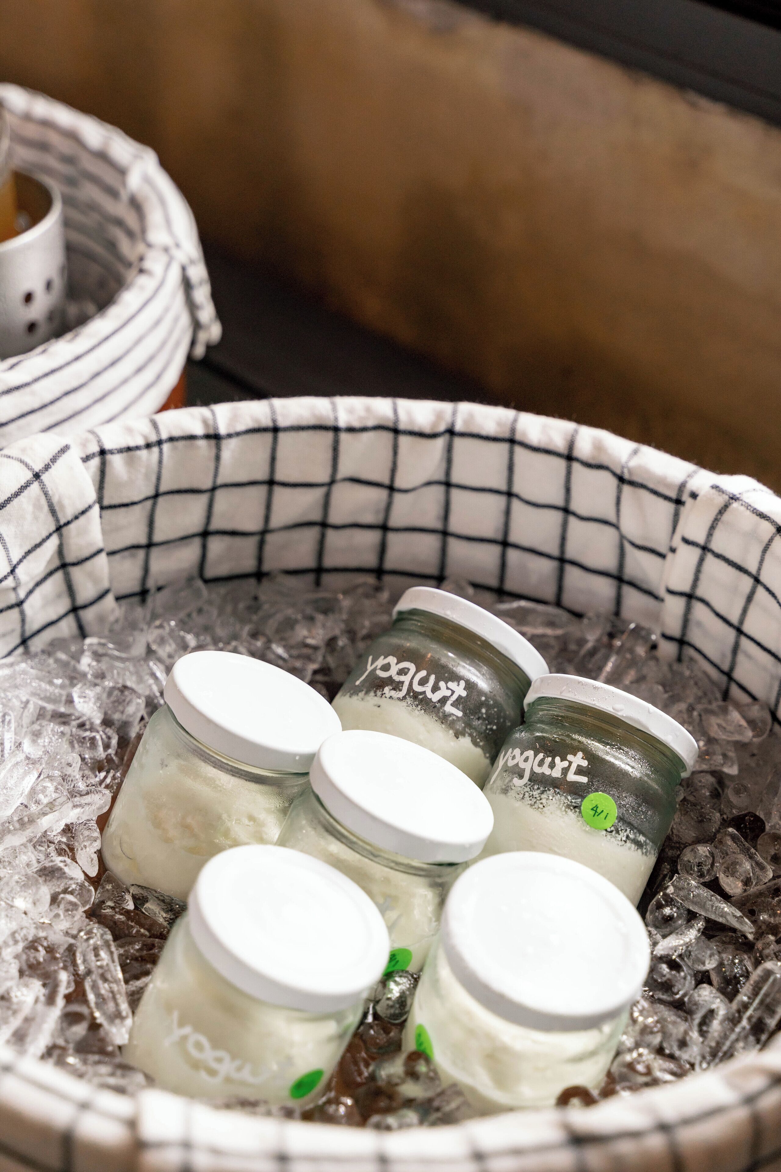 Una cesta llena de hielo y varios frascos de vidrio etiquetados como 'yogurt'.