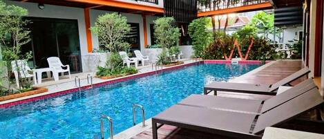 An indoor swimming pool with lounge chairs and a covered area with a balcony.