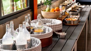 A buffet setup with various food items and drinks, arranged on a long table with a view of greenery outside. - WOW PHUKET (Chalong)