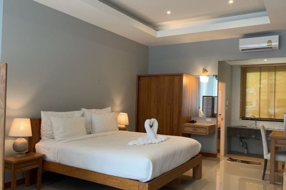 A hotel room with a wooden bed, bedside tables with lamps, a desk, and an air conditioning unit.