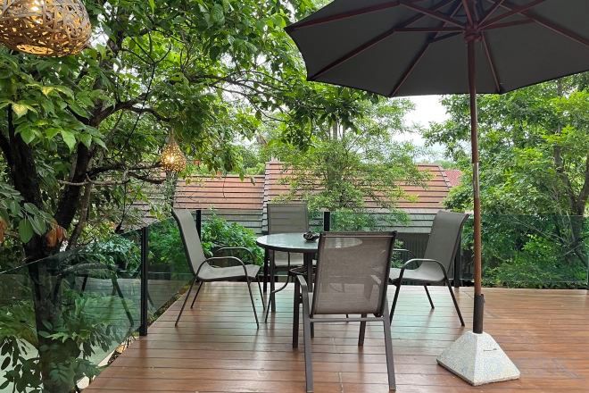An outdoor patio with a table and chairs, surrounded by glass railings and greenery.