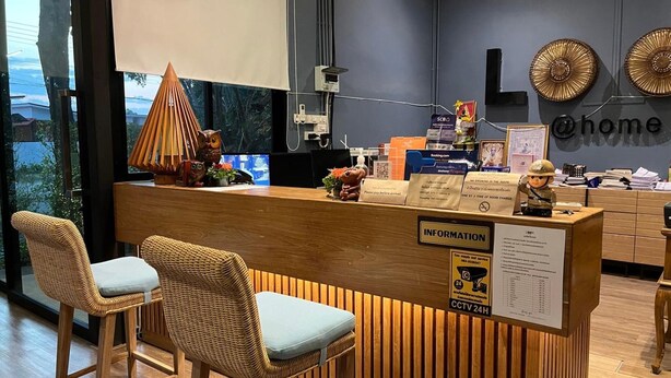 A reception desk with a wooden counter, two wicker chairs, a decorative lamp, and a view of the outdoors. - Look At Home Lamphun (Lamphun)