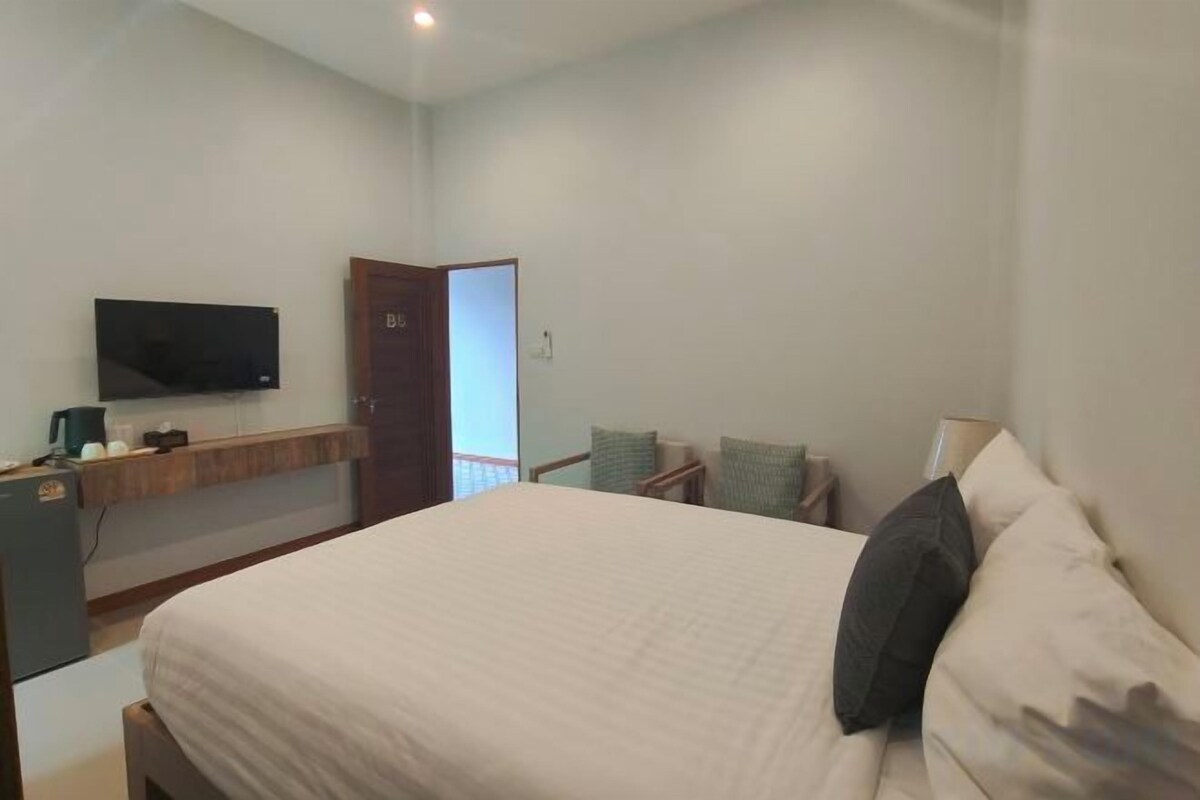 A bedroom with a bed, a television on the wall, a door, and a small table with a lamp.