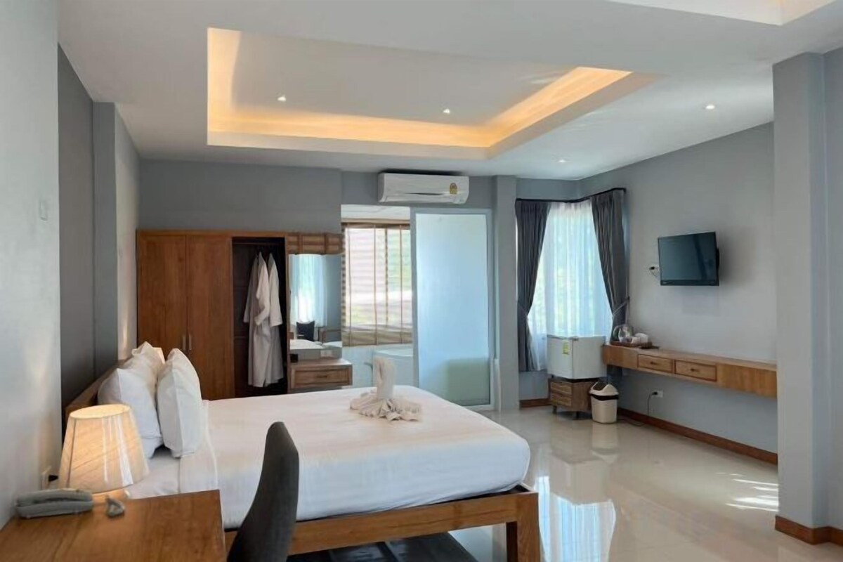 A modern hotel room with a bed, bedside table, lamp, and a TV mounted on the wall.