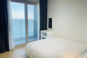 A hotel room with a bed, a small white nightstand, a mirror, and a view of the sea through a sliding glass door. - OceanStay E7 INN-The City jukdo (Yangyang)