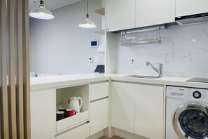 Une cuisine moderne avec des meubles blancs, un lave-linge encastré et des luminaires suspendus.