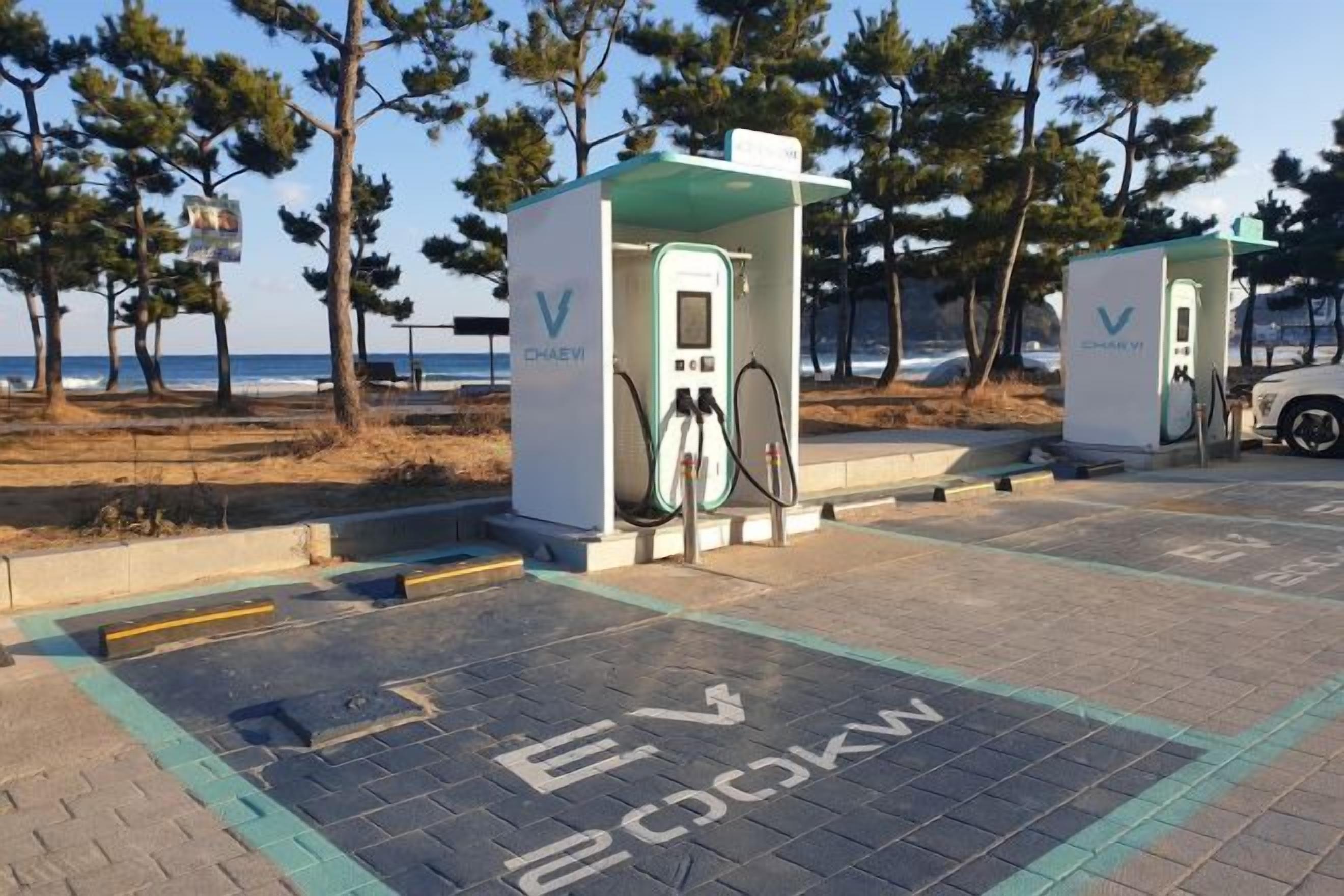 Electric vehicle charging stations with a clear view of the beach and trees in the background.