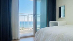 Une chambre d’hôtel avec un grand lit, une vue sur l’océan et un balcon doté d’une balustrade.