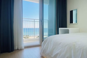 A hotel room with a large bed, a view of the ocean, and a balcony with a railing. - OceanStay E7 INN-The City jukdo (Yangyang)
