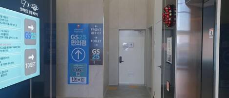 Un pasillo de hotel con un cartel digital, un letrero azul para la recepción y los baños, y un extintor en la pared.