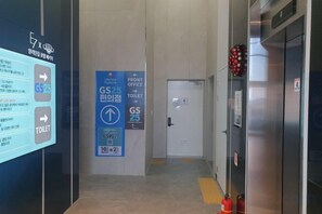 A hotel corridor with a digital signboard, a blue sign for the front office and toilet, and a fire extinguisher on the wall. - OceanStay E7 INN-The City jukdo (Yangyang)