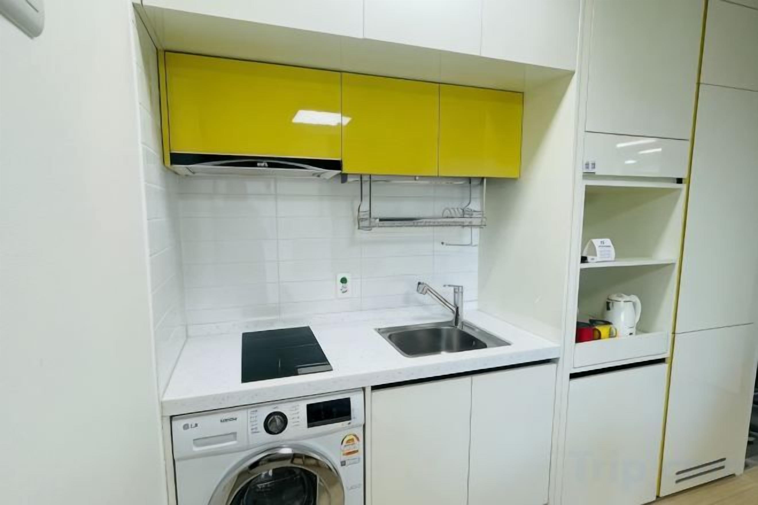 Une cuisine équipée d’un lave-linge, d’un évier et de meubles de rangement jaunes.