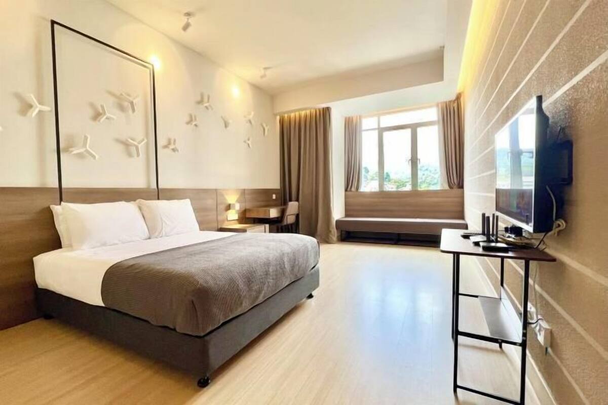 A modern hotel room with a bed, bedside table, TV, and a large window.