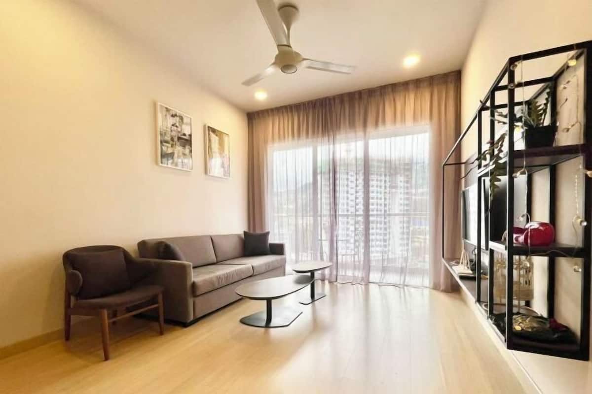 A living room with a sofa, a chair, a small table, a ceiling fan, and a bookshelf.
