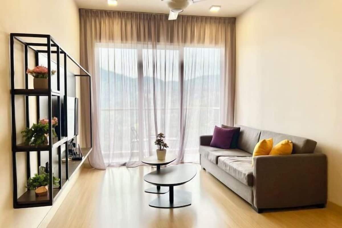 A living room with a sofa, a coffee table, a bookshelf, and a large window with curtains.