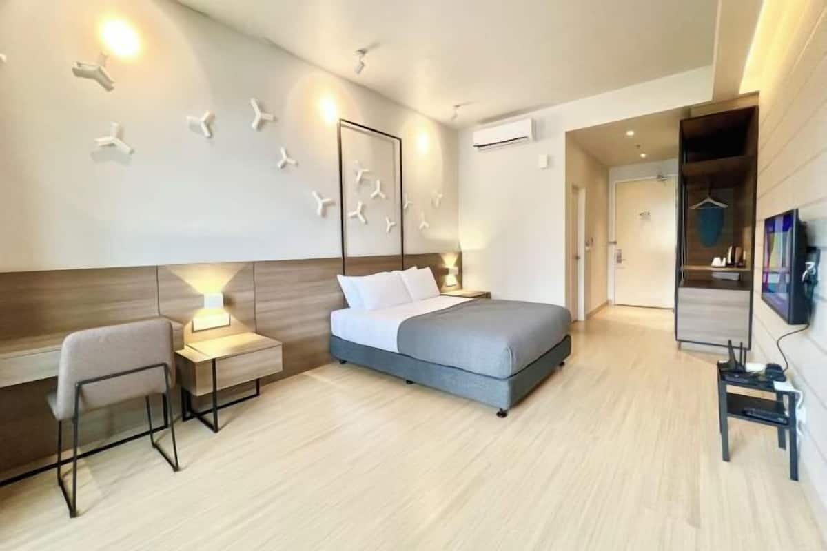 A modern hotel room with a bed, bedside table, chair, and a TV.