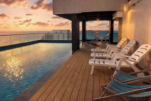 Zona junto a la piscina con sillas de descanso y vista al océano.