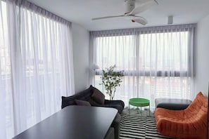 A modern living room with a sofa, a green side table, a black coffee table, and a ceiling fan. - The guestrooms (Pattaya)
