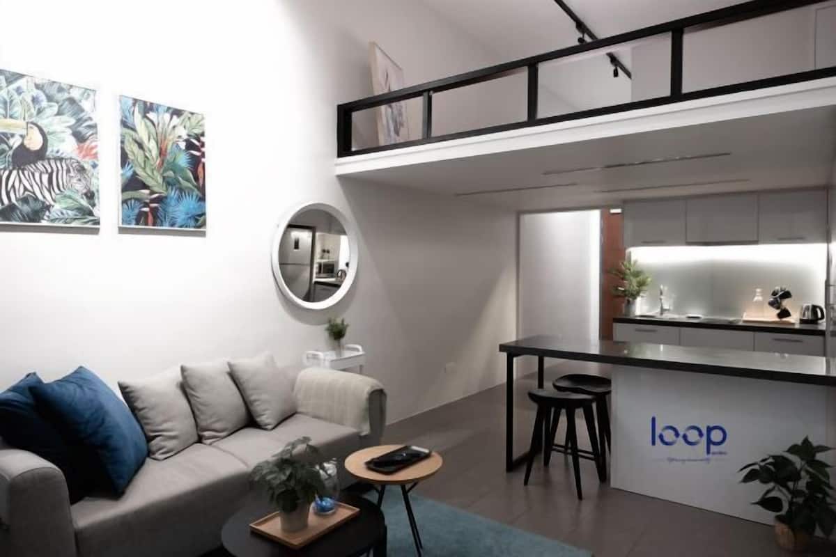 A modern living space with a sofa, a small round table, a kitchen area, and a dining table with stools.