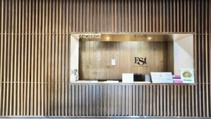 A reception desk with a wooden panel design, a sign reading 'ONCIERGE,' and a logo with 'ES' in the center. - KL Sentral Serviced Apartment - The Establishment KL Sentral by Loop Suites (Kuala Lumpur)