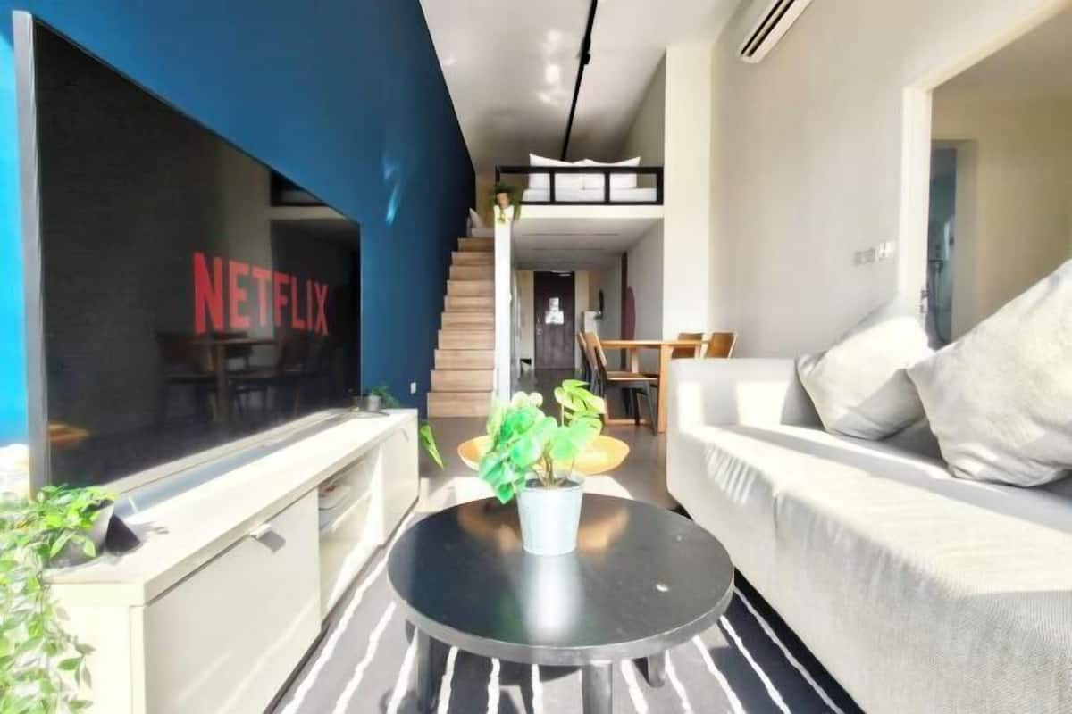 A modern living room with a sofa, a coffee table with a plant, a staircase, and a visible Netflix logo on a window.