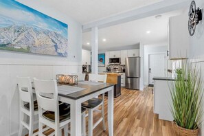 A modern kitchen with white cabinets, a stainless steel refrigerator, and a dining area with white chairs and a wooden table.
