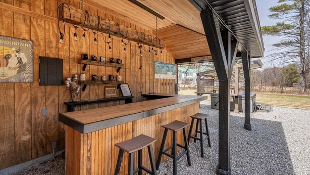 Zona de bar rústica de madera con taburetes, estantes con vasos y un mapa en la pared.