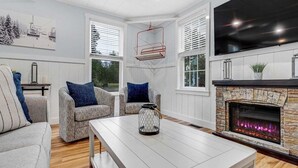 Una sala de estar con chimenea, sillones estampados, una mesita de centro y un televisor grande.