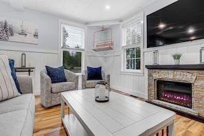 A living room with a fireplace, patterned chairs, a coffee table, and a large TV.