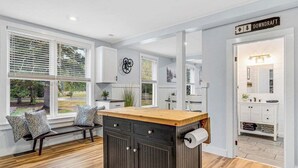 Una cocina moderna con una isla central, armarios blancos y ventanas amplias.