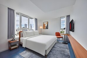 Une chambre d’hôtel avec un grand lit, un bureau, une chaise, une télévision et une vue sur la ville.